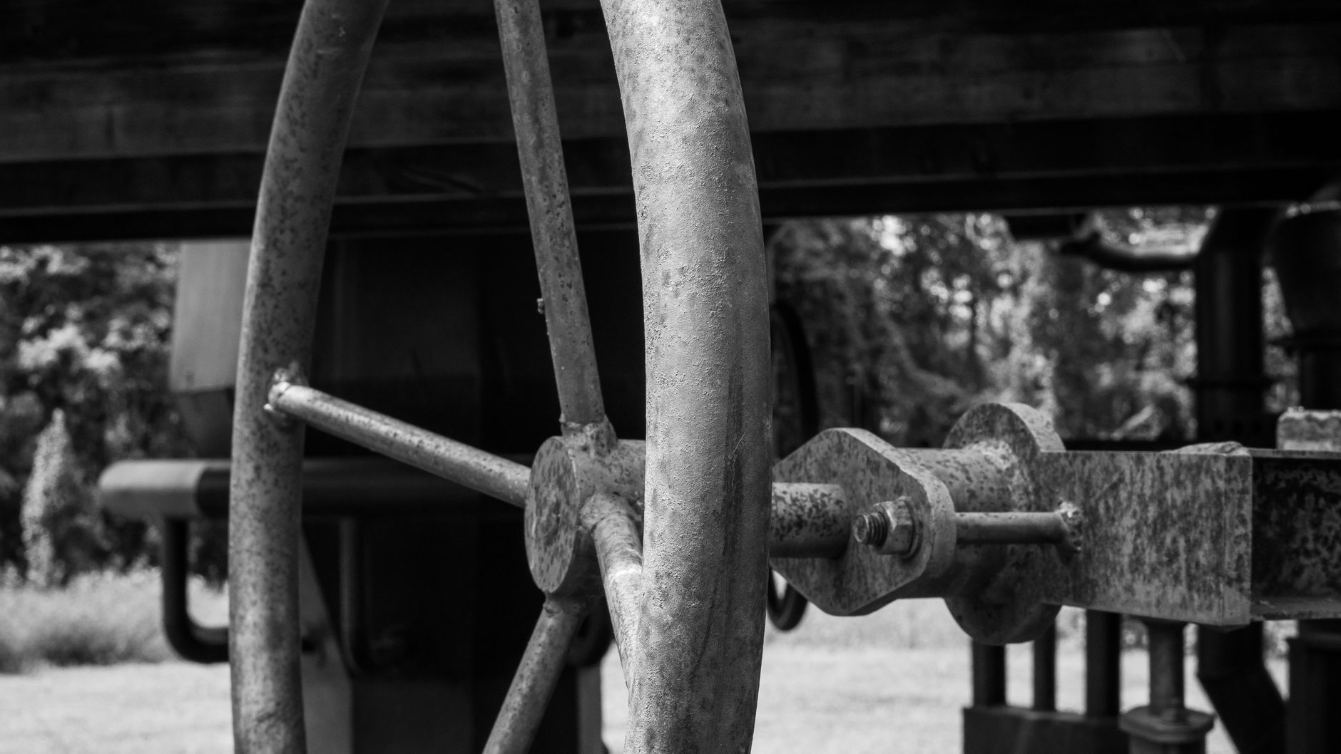 Close-up of a rusty metal wheel on industrial machinery in a black and white setting.