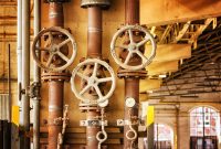 aap-corrosion-resistant-material-selection-for-chemical-plant-piping-1791122444 Close-up of rusty industrial pipes and valves, showcasing aging machinery in a factory setting.