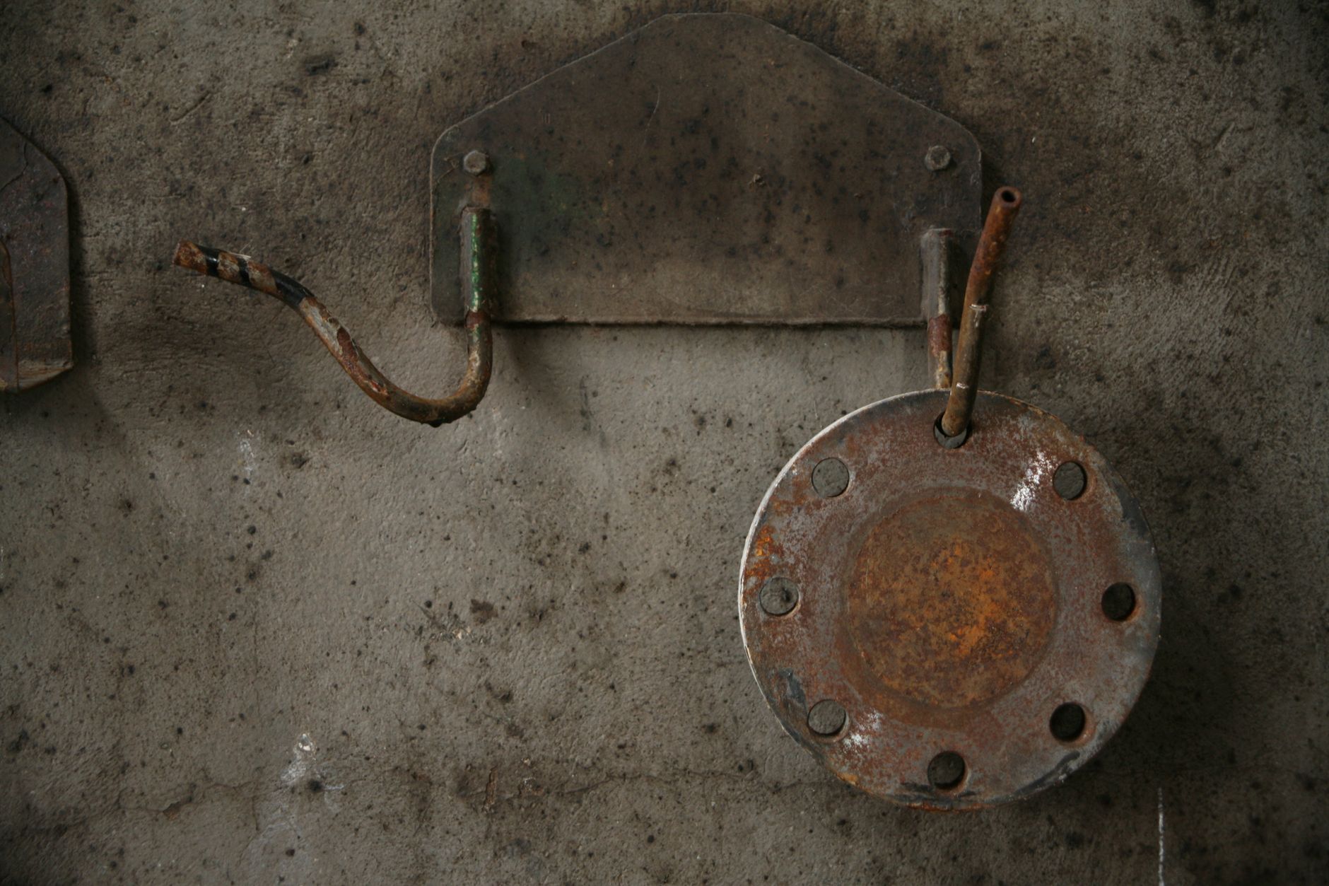 Rusty metal fixtures on a weathered concrete wall, showcasing industrial decay.