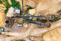 aap-how-to-calculate-conveyor-belt-tension-for-bulk-material-handling-1791040211 Top-down view of a sprawling industrial mining site featuring heavy machinery and detailed terrain.