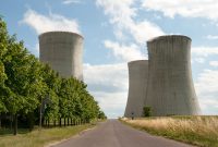 A nuclear power plant cooling towers by a road with green trees under a clear sky.